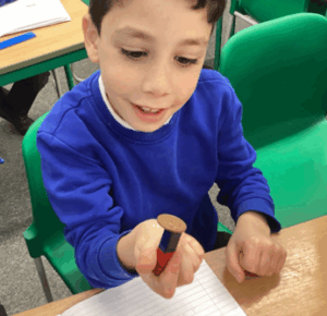 A boy in a blue sweater holding up a small bar magnet with a metallic disc attached to the end.